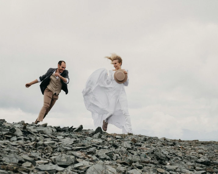 a man and a woman running on a rocky hill, an album cover, by Lee Loughridge, pexels contest winner, happening, bride and groom, white, thumbnail, actors