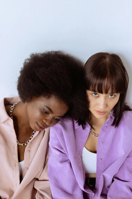 a couple of women sitting next to each other, an album cover, by Nina Hamnett, trending on pexels, synchromism, whitebangsblackhair, concerned, pastels, purple