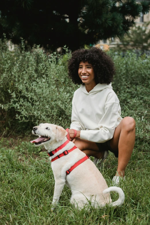 a woman kneeling in the grass with a dog, trending on unsplash, african american young woman, wearing a red hoodie, an all white human, collar and leash