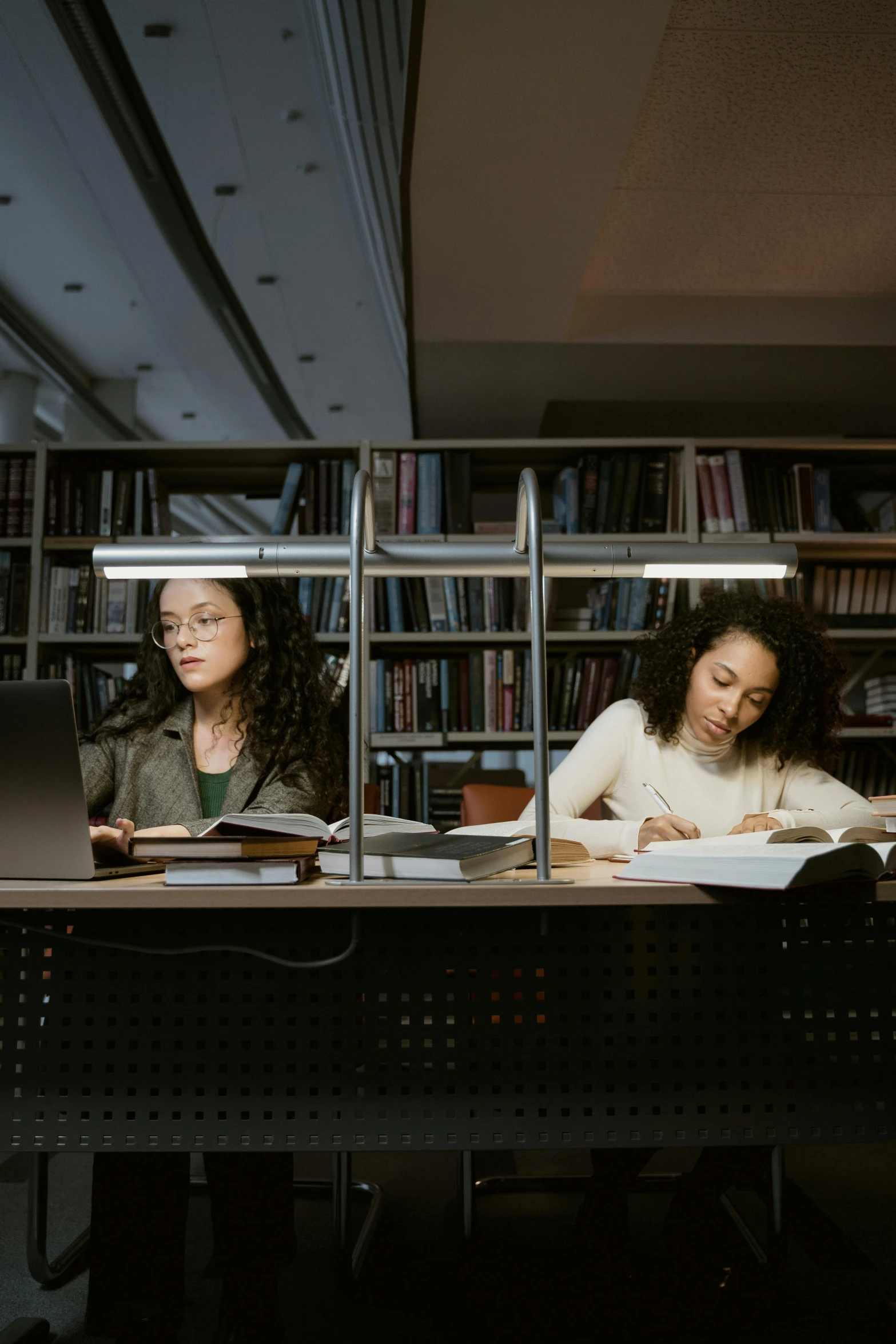 a couple of women sitting at a table in a library, pexels contest winner, academic art, slight overcast lighting, computer science, an olive skinned, flying books