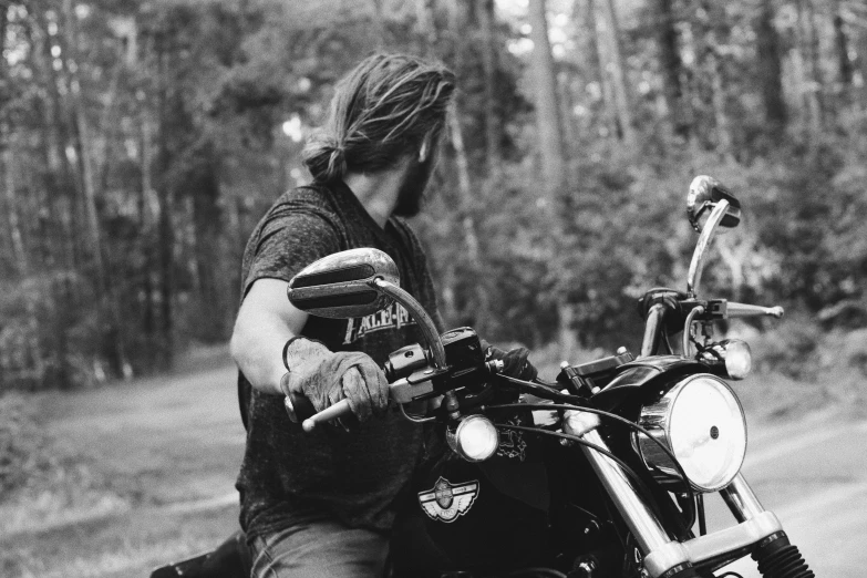 a man riding on the back of a motorcycle down a road, a black and white photo, pexels, lumberjack, holding helmet, profile pic, dread