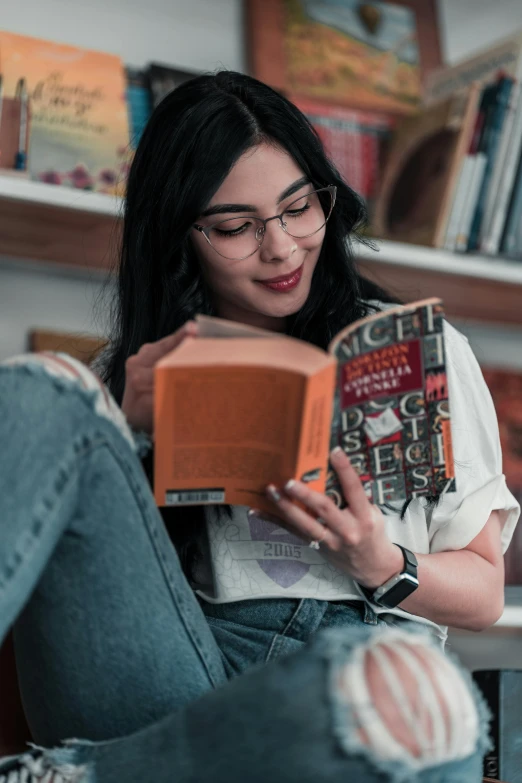 a woman sitting in a chair reading a book, a cartoon, pexels contest winner, wavy long black hair and glasses, jeans and t shirt, gif, bookshops