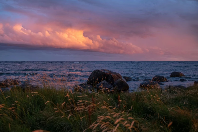 a couple of rocks sitting on top of a lush green field, by Jesper Knudsen, unsplash, at beach at sunset, pink storm clouds, offshore winds, fire on the horizon