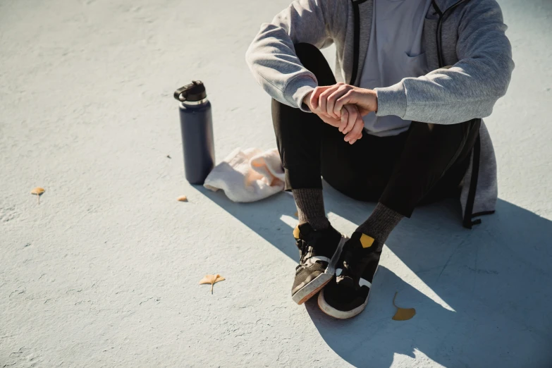 a man sitting on top of a skateboard next to a water bottle, trending on pexels, sitting with wrists together, destitute, grey clothes, slightly sunny