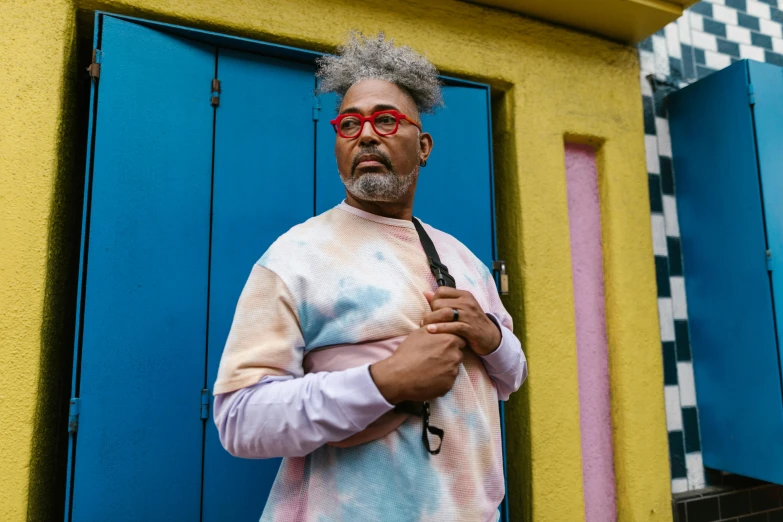 a man in a tie dye shirt holding an umbrella, an album cover, inspired by Howardena Pindell, pexels contest winner, leaning on door, in sao paulo, wearing small round glasses, messy curly pastel hair