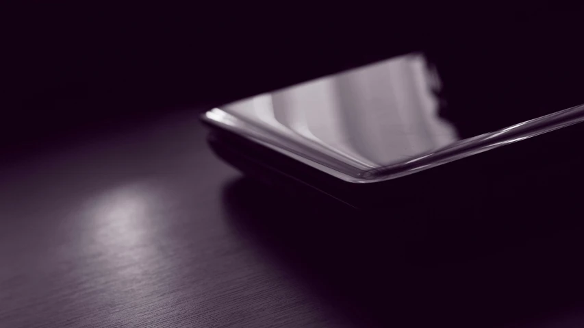 a cell phone sitting on top of a wooden table, a black and white photo, unsplash, minimalism, purple ambient light, lacquered glass, close up photograph, angled shot