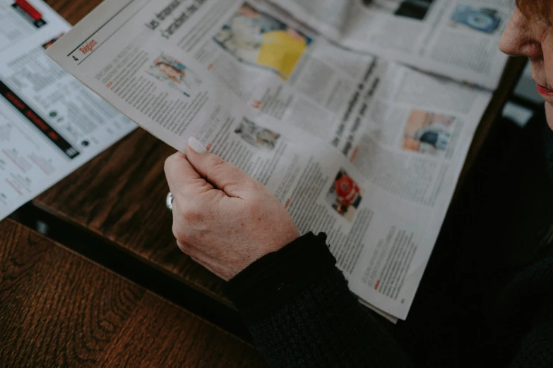 a woman sitting at a table reading a newspaper, unsplash, holding it out to the camera, holding an epée, listing image, middle close up shot