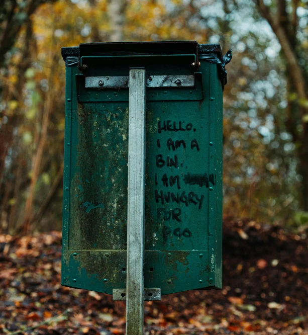 a green trash can sitting in the middle of a forest, an album cover, by Elsa Bleda, unsplash, graffiti, letterbox, autumnal, hungry, hello world