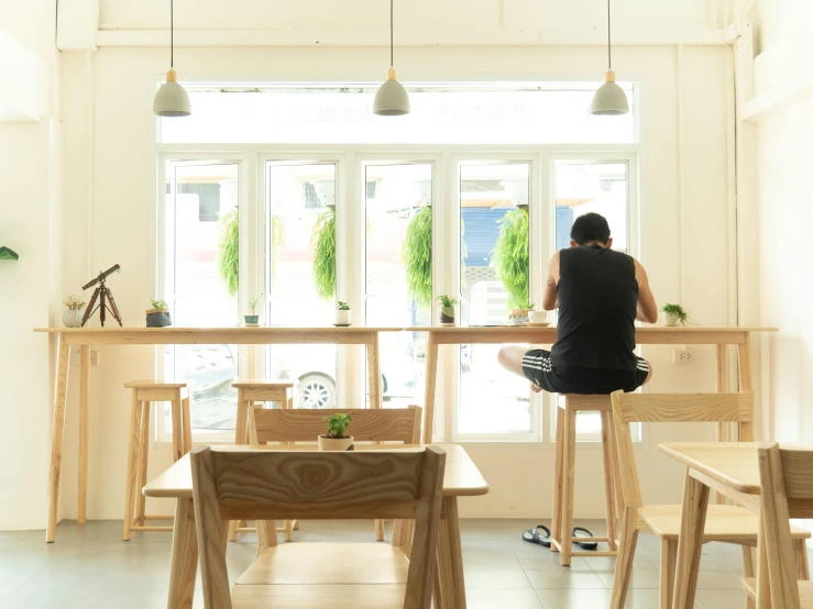 a person sitting at a table in a room, unsplash, light and space, small hipster coffee shop, outram, hoang lap, minimalist furniture