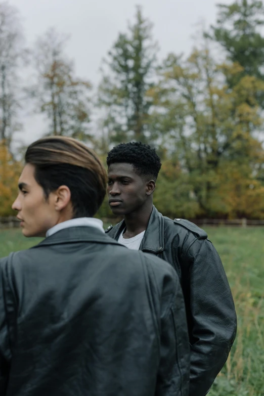 two men standing next to each other in a field, trending on pexels, visual art, she wears leather jacket, black teenage boy, pompadour, color footage