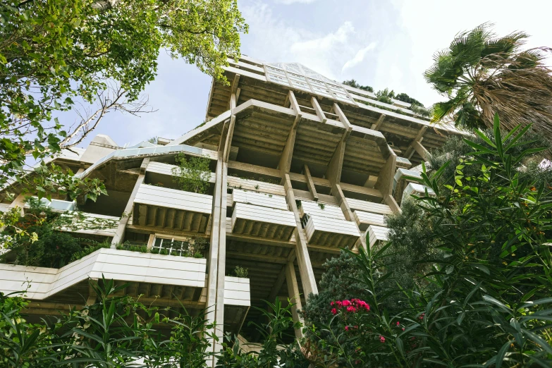 a tall building sitting in the middle of a lush green forest, brutalism, plants on balconies, houses on stilts, view from the ground, conde nast traveler photo