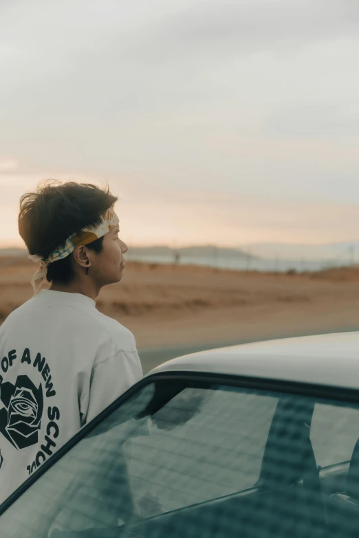 a man standing next to a car on a road, an album cover, unsplash contest winner, wearing a headband, gazing off into the horizon, profile image, teen boy