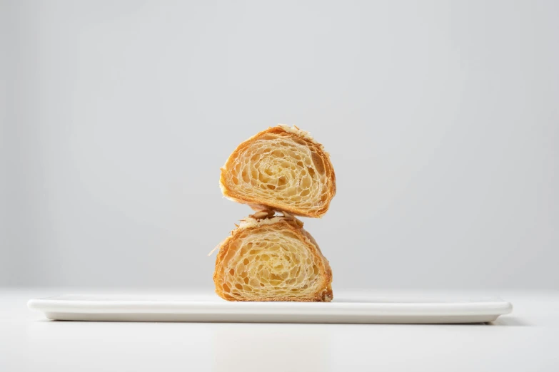 two croissants stacked on top of each other on a plate, inspired by Géza Dósa, unsplash, art nouveau, on white background, light lighting side view, crushed, miniature product photo