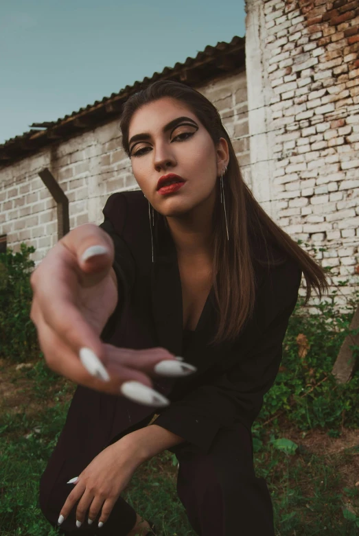 a woman holding a cigarette in one hand and a cigarette in the other, an album cover, inspired by Elsa Bleda, trending on pexels, villain pose, hand gesture, outdoor photo, androgynous vampire