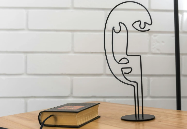 a book sitting on top of a table next to a lamp, inspired by Alexander Archipenko, pexels contest winner, new sculpture, man with thin lines on the face, armature wire, on a candle holder, curving black