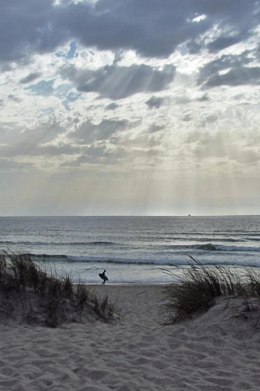 a person riding a surfboard on top of a sandy beach, by Joe Stefanelli, sunrays between clouds, dunes, tyndall rays, “ iron bark