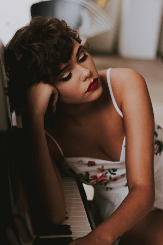 a woman sitting on the floor next to a piano, a picture, inspired by Elsa Bleda, trending on pexels, pouty lips, isabela moner, curly bangs, profile image