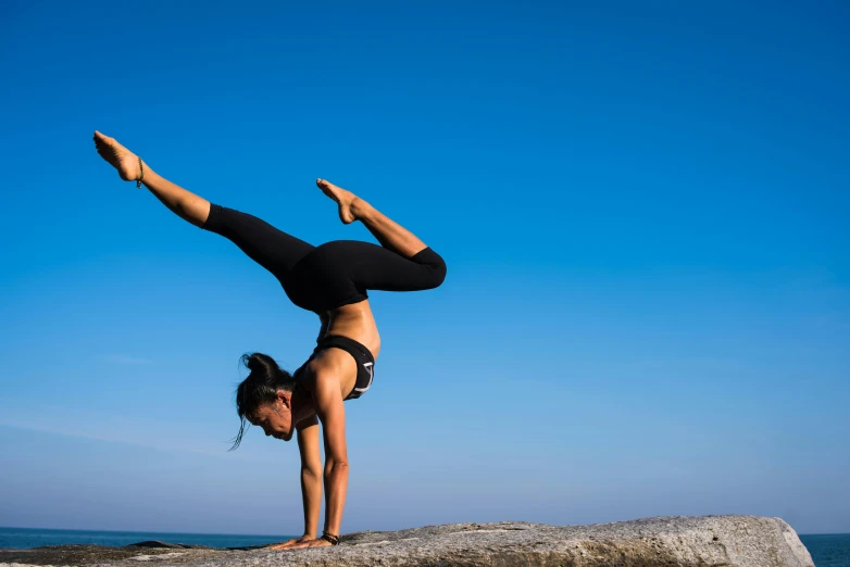 a woman doing a handstand on a rock by the ocean, pexels contest winner, arabesque, relaxed. blue background, profile image, working out, spinning hands and feet