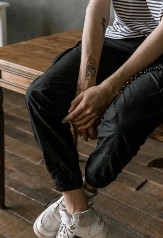 a man sitting on top of a wooden bench, trending on pexels, photorealism, black sweatpants, seated at a table, wearing cargo pants, high details photo