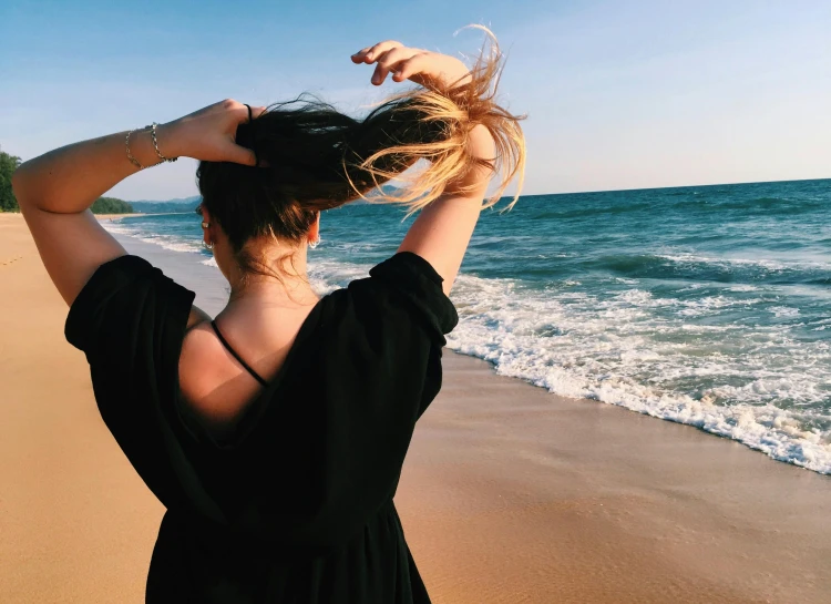 a woman standing on top of a beach next to the ocean, pexels contest winner, happening, back of the hair, hair fanned around, various posed, profile image