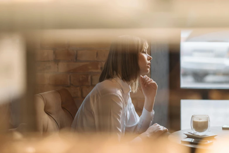 a woman sitting at a table with a cup of coffee, trending on unsplash, looking through a window frame, pondering, people at work, ilustration