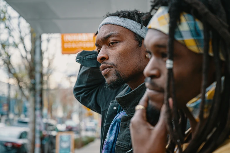 a man standing next to a woman on a cell phone, a photo, trending on pexels, black arts movement, gang saints wear yellow bandanas, looking into the distance, dreads, [ theatrical ]