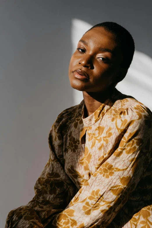 a woman sitting on a chair in a room, trending on unsplash, renaissance, wearing yellow floral blouse, dark skin tone, androgynous face, a portrait of issey miyake