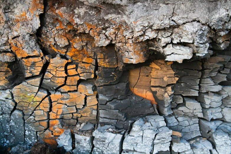 a close up of a piece of wood with orange lichen on it, an album cover, by Koloman Sokol, unsplash, chiseled formations, cracks of magma, with lots of dark grey rocks, pixel degradation