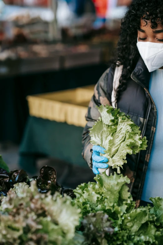 a woman wearing a face mask holding a bunch of lettuce, by Matt Cavotta, trending on pexels, renaissance, market setting, wearing gloves, blue, black