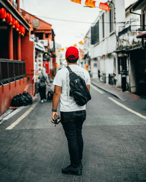 a man with a backpack walking down a street, pexels contest winner, lgbt, red cap, graphic tees, asian human