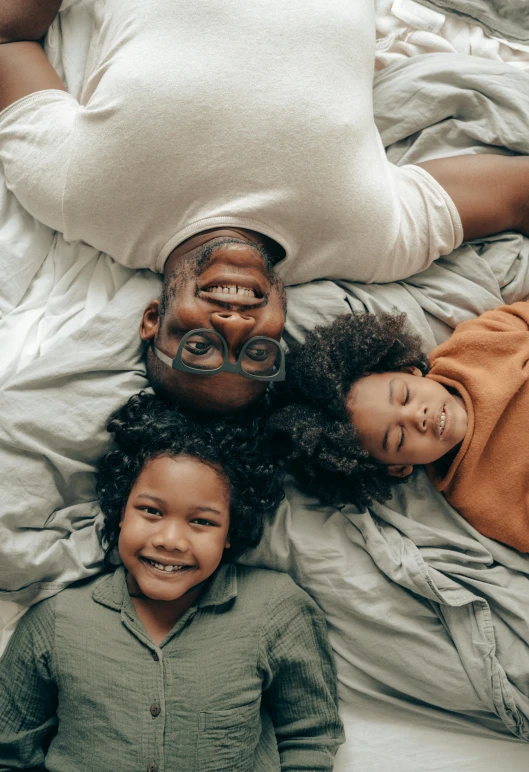 a group of people laying on top of a bed, by Carey Morris, pexels contest winner, incoherents, caring fatherly wide forehead, large black smile, portrait of family of three, high definition screenshot