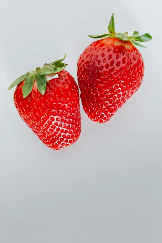 two strawberries sitting next to each other on a white surface, profile image, digital image, front facing, uncrop