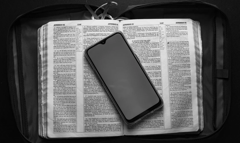 a cell phone sitting on top of an open book, a black and white photo, by Carey Morris, pexels, unilalianism, christianity, full length photo, biblical image, contain