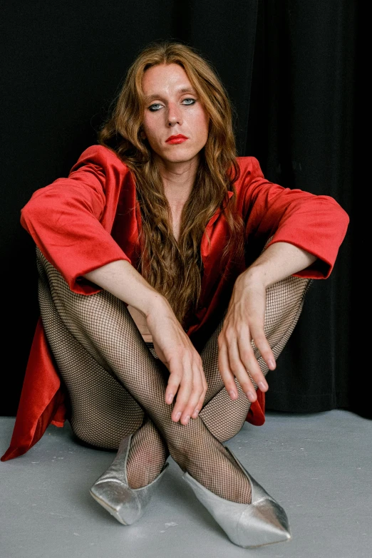 a woman sitting on the floor with her legs crossed, an album cover, inspired by Cindy Sherman, renaissance, red tailcoat, long hair and red shirt, taken in 2 0 2 0, transgender