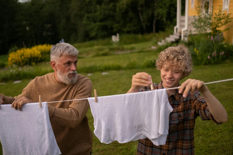 a man and a woman hanging out clothes on a clothes line, by Jaakko Mattila, pexels contest winner, symbolism, father with child, older male, bo burnham, wearing a linen shirt