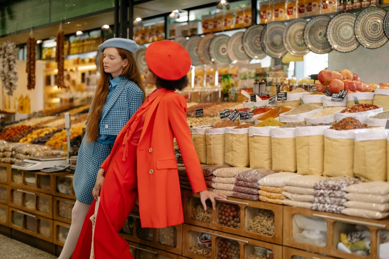 a couple of women standing next to each other, by Julia Pishtar, trending on pexels, maximalism, shopping groceries, in the style wes anderson, red tailcoat, bakery