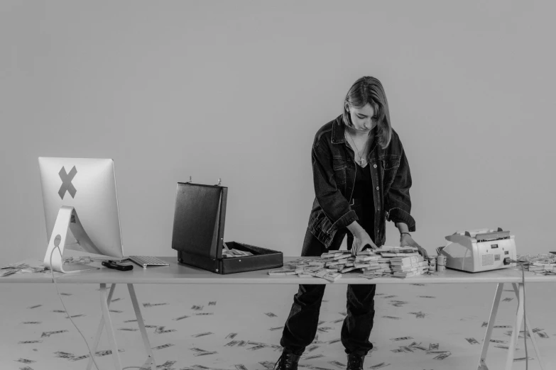 a woman that is standing in front of a table, a black and white photo, creative coder with a computer, with piles of coins around it, in a gallery setting, resembling a mix of grimes