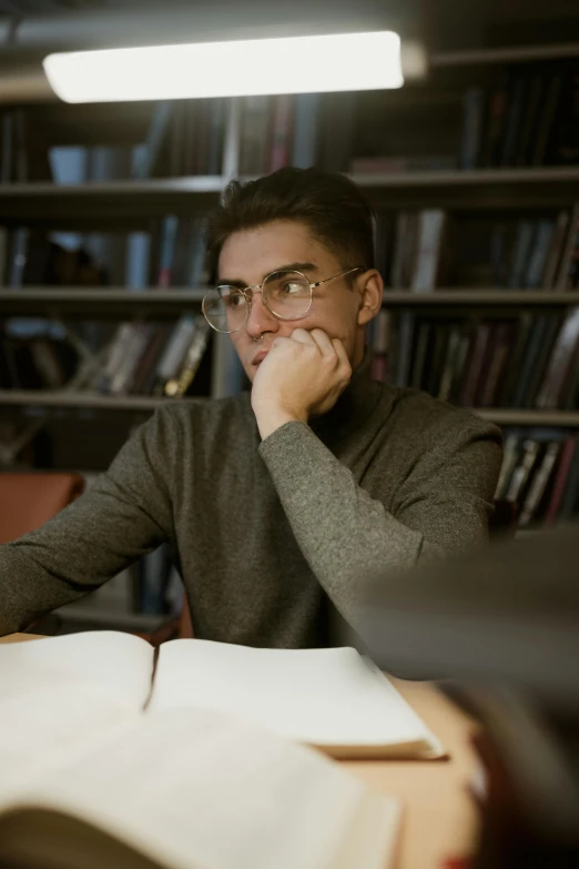 a man sitting at a table with a book in front of him, reddit, academic art, unibrow, thoughtful ), candid photograph, student