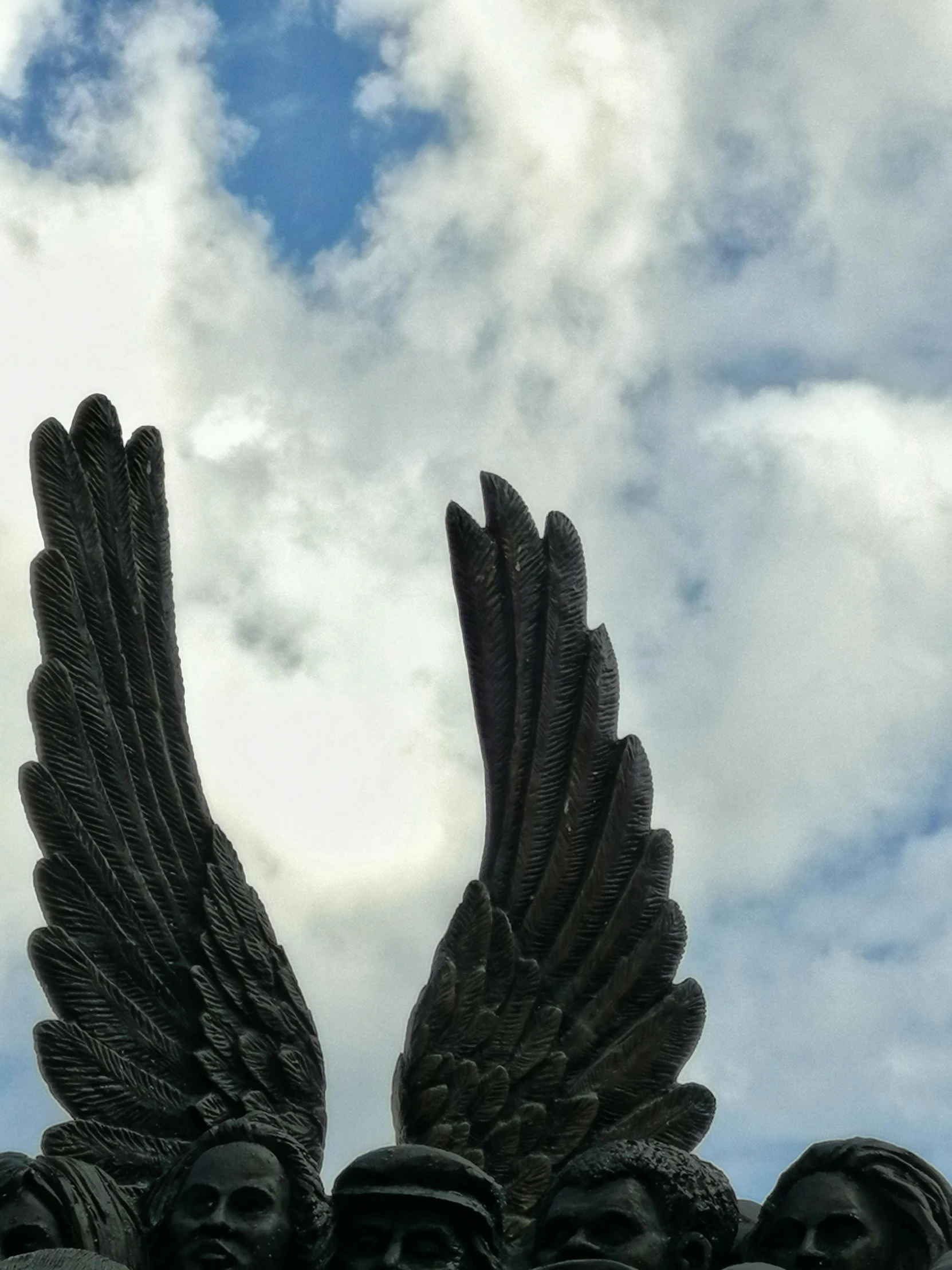 a statue of a group of people with wings, by Carey Morris, unsplash, hurufiyya, very detailed black feathers, sky view, close up shot from the side, low quality photo
