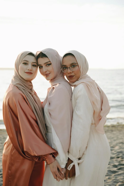 three women standing next to each other on a beach, inspired by Maryam Hashemi, unsplash, hurufiyya, hijab, light blush, attractive girl, malaysian