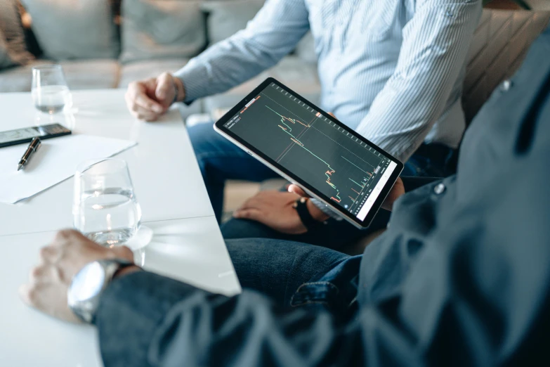 a couple of people sitting at a table with a tablet, trending on unsplash, renaissance, displaying stock charts, “ iron bark, business meeting, background image