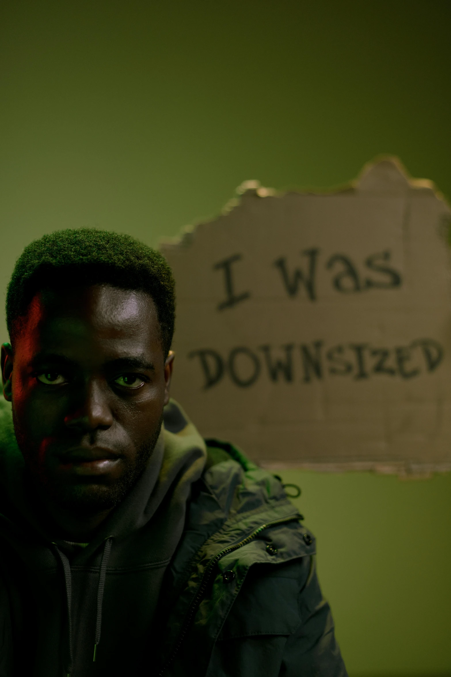 a man sitting in front of a sign, pexels contest winner, movie still of a tired, godwin akpan, green doom guy, oppression