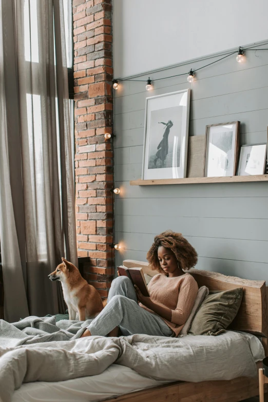 a woman sitting on top of a bed next to a dog, reading nook, cozy lights, african american young woman, top selection on unsplash