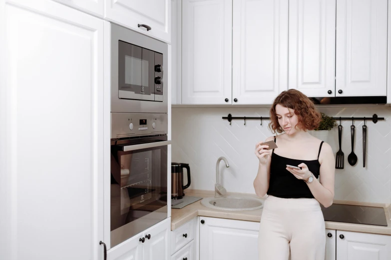 a woman standing in a kitchen looking at her cell phone, trending on pexels, white, ekaterina, slightly minimal, low quality photo