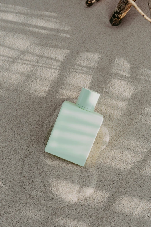 a bottle of perfume sitting on the ground, inspired by Raoul De Keyser, unsplash, conceptual art, celadon glaze, square, sunbathed skin, product view