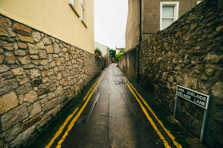 a narrow street with a sign on the side of it, by Andrew Allan, unsplash, holywood scene, yellow, stone roads, leesha hannigan