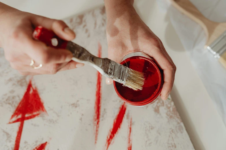 a close up of a person holding a paint brush, red liquid, red and white marble panels, candle wax, white wall coloured workshop