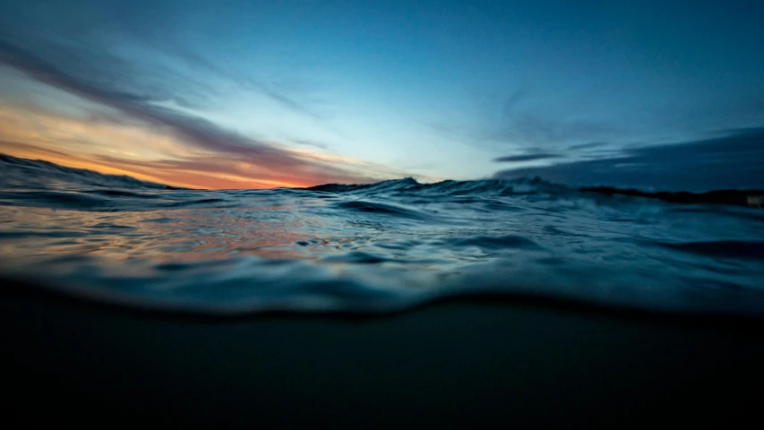 a body of water with a sunset in the background, by Niko Henrichon, unsplash, blue crashing waves, water line surface, up close, daniel richter