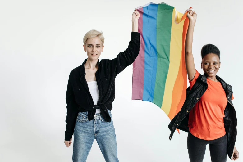 two women standing next to each other holding a rainbow flag, a photo, trending on pexels, on clear background, androgyny, flag in hands up, a blond