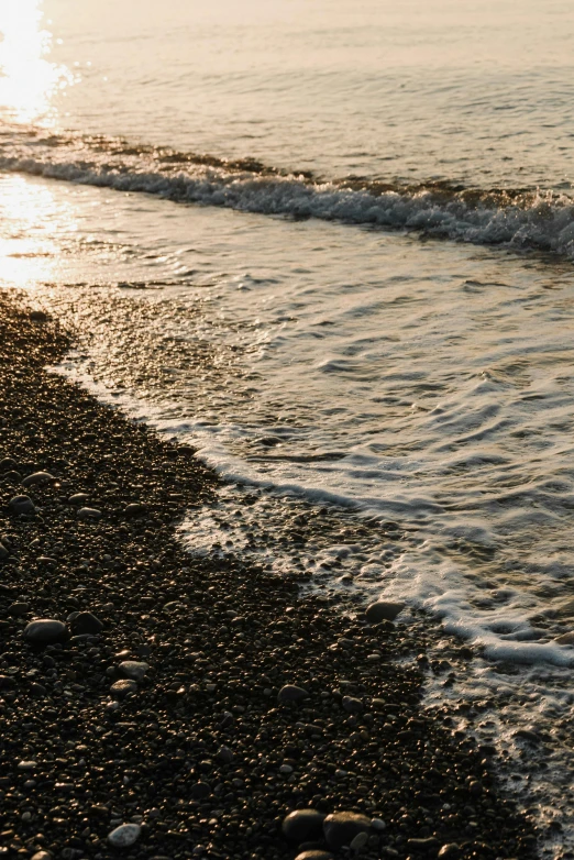 a person riding a surfboard on top of a sandy beach, coral-like pebbles, black sea, dappled in evening light, slide show